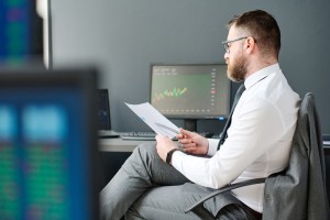 Young adult man with beard on face sitting at desk in office working on investment business strategy