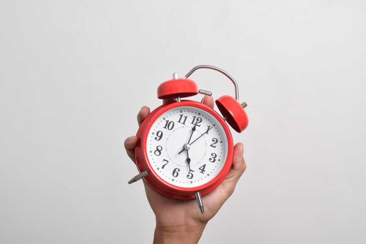 Vintage red alarm clock in hand. Round red alarm clock isolated on white background shows 5 am.