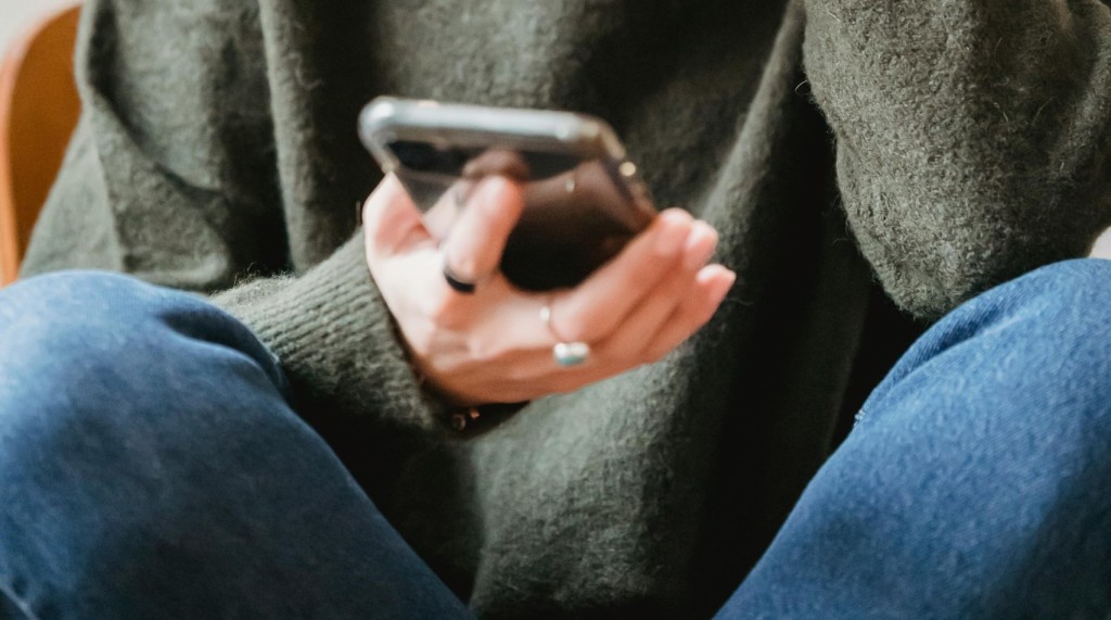 Person wearing a sweater holds a smartphone